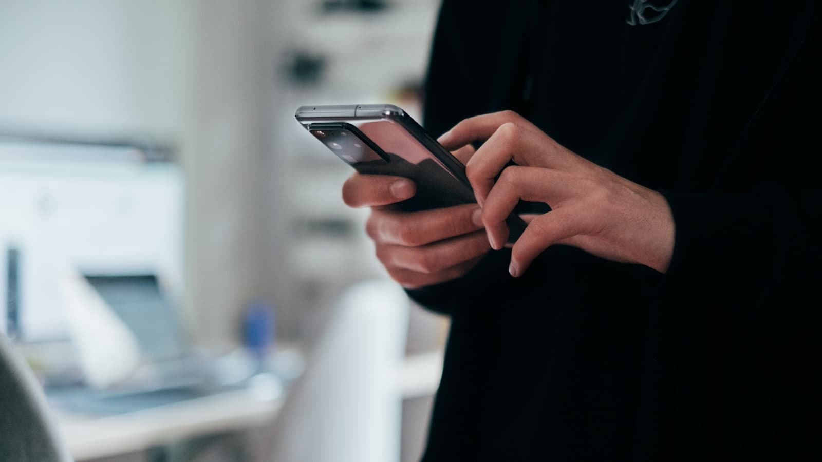 Une personne tient un smartphone Android noir à deux mains, écran allumé.