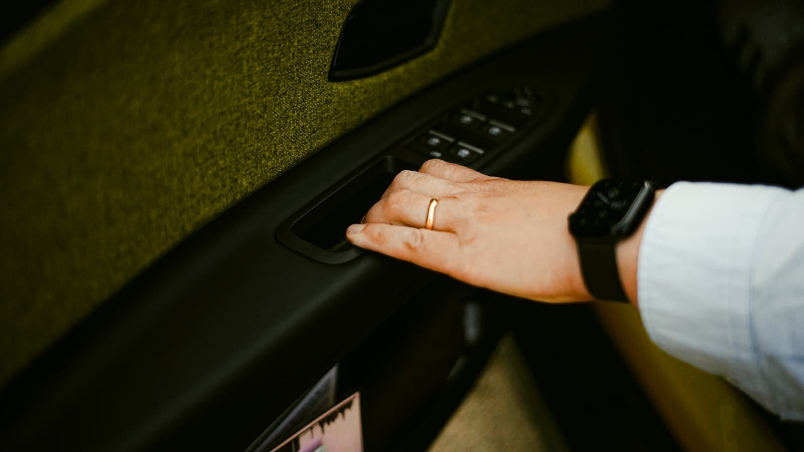 Main ouvrant une portière de voiture depuis l'intérieur, près des commandes de vitres.