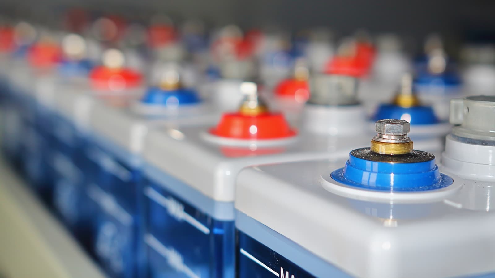 Rangées de batteries industrielles alignées, bornes rouges et bleues.