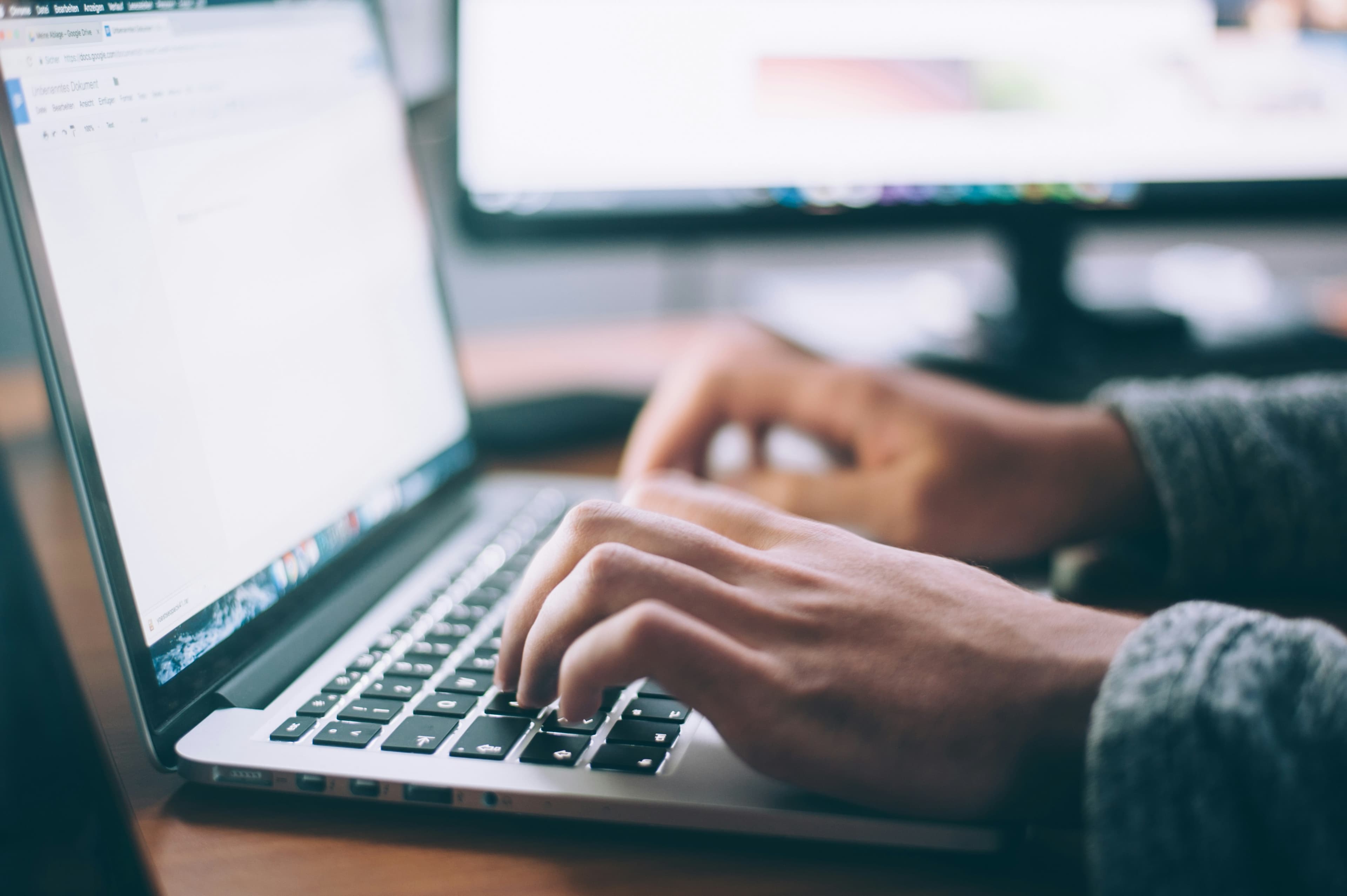 Une personne tape sur le clavier d'un ordinateur portable posé sur un bureau en bois.