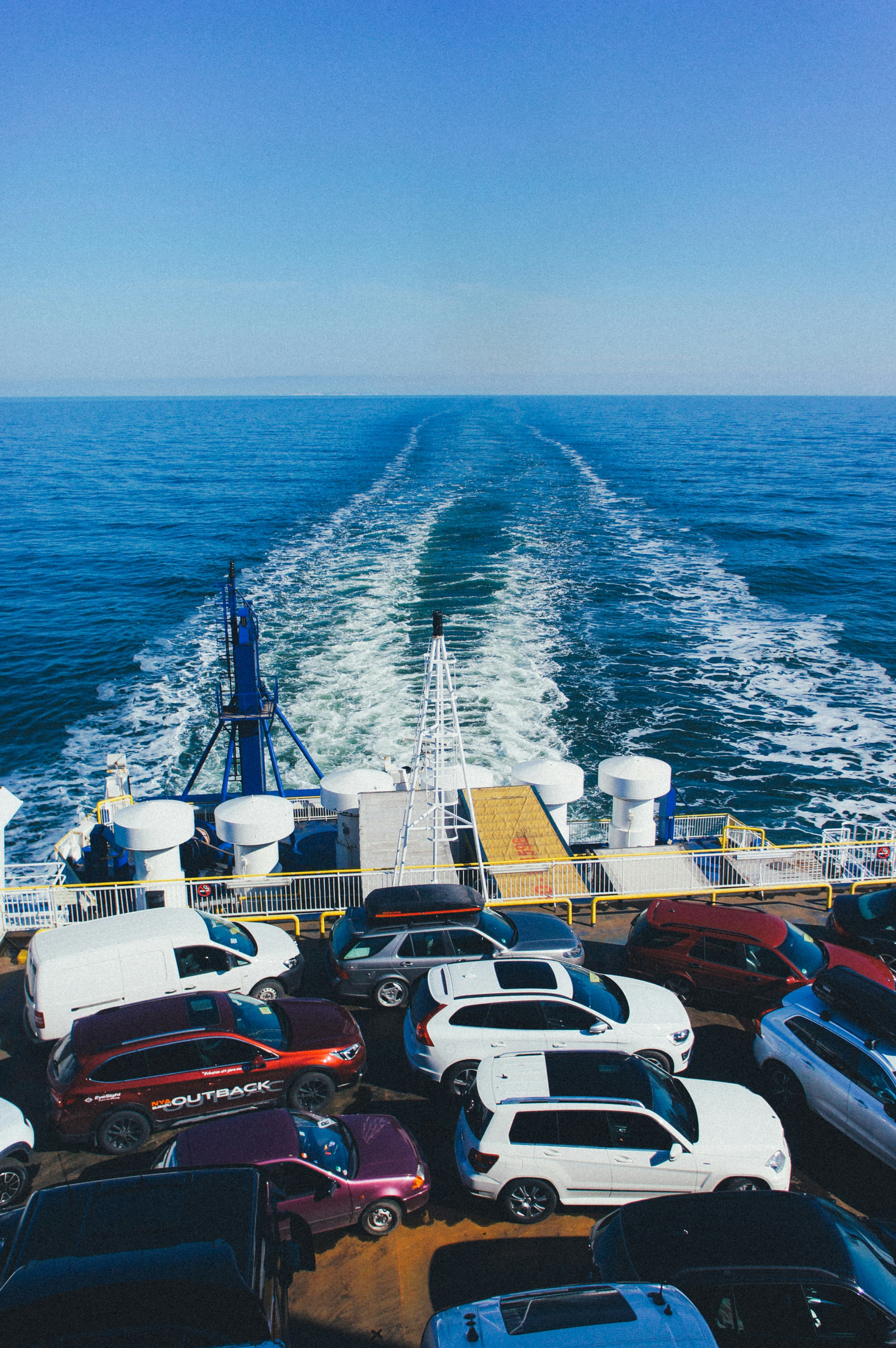 Véhicules empilés sur le pont d'un navire cargo au large, sous un ciel bleu.