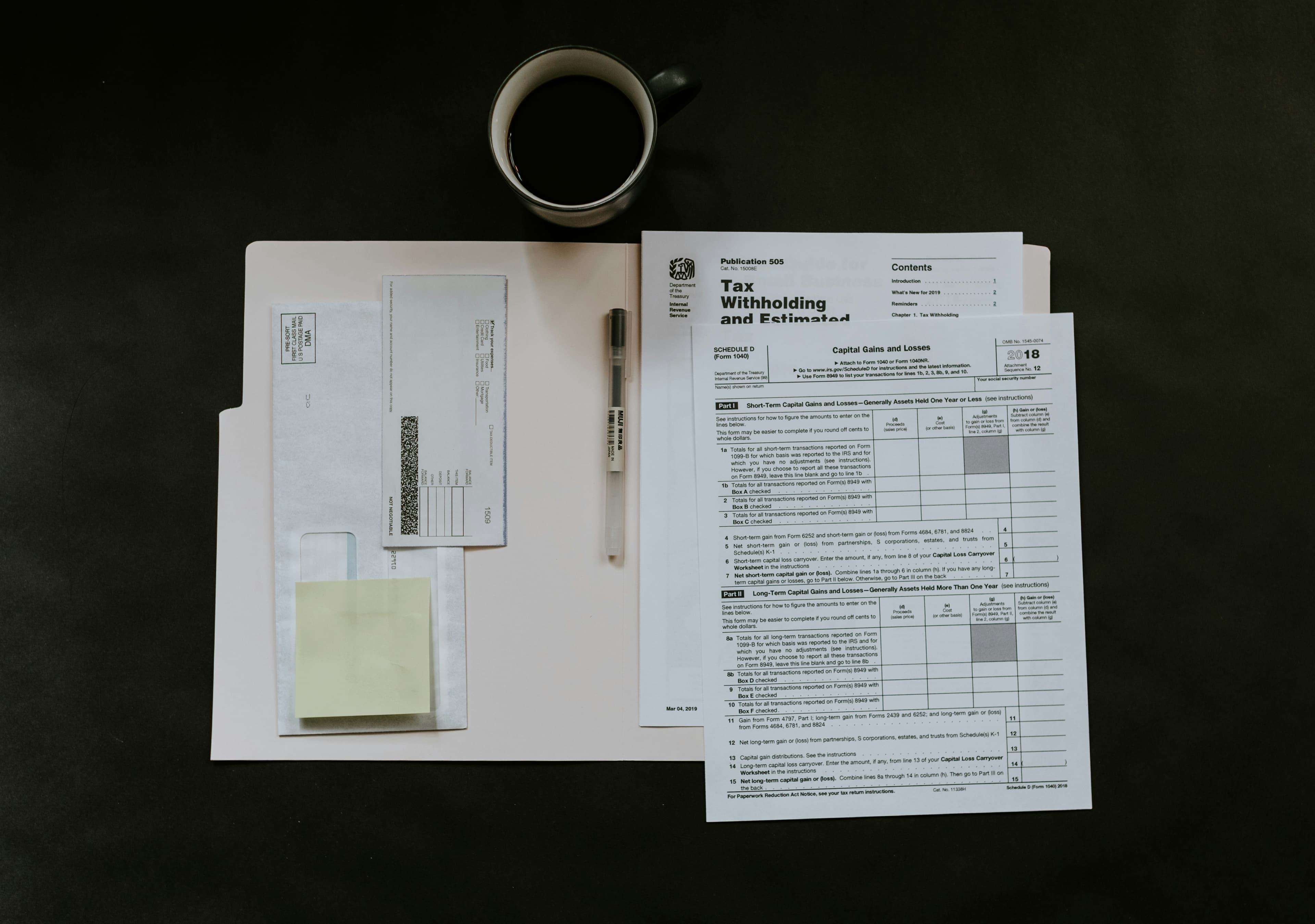 Des formulaires fiscaux, un stylo et une tasse de café sur un bureau sombre