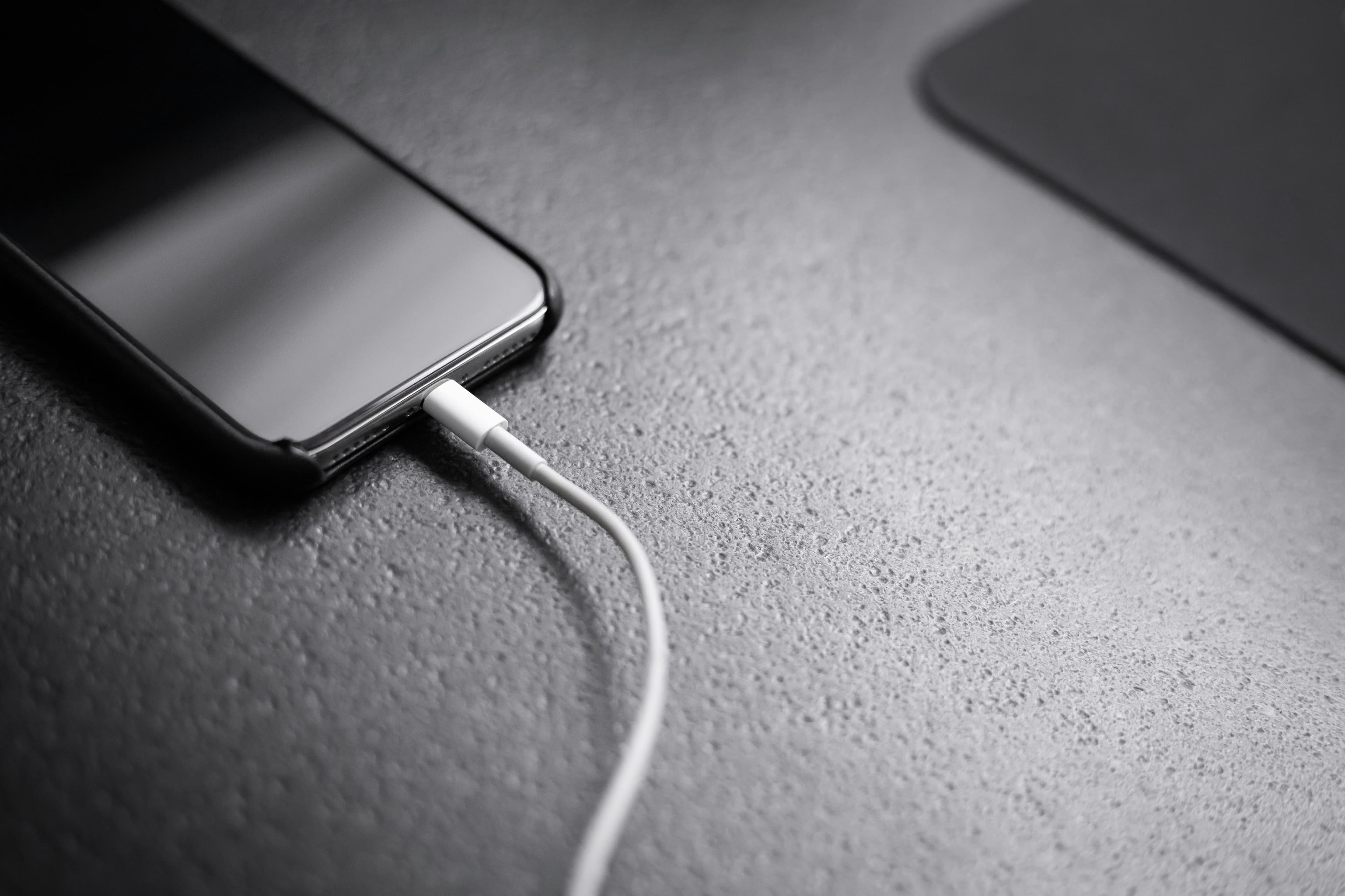 Smartphone noir posé sur une surface, connecté à un câble de recharge