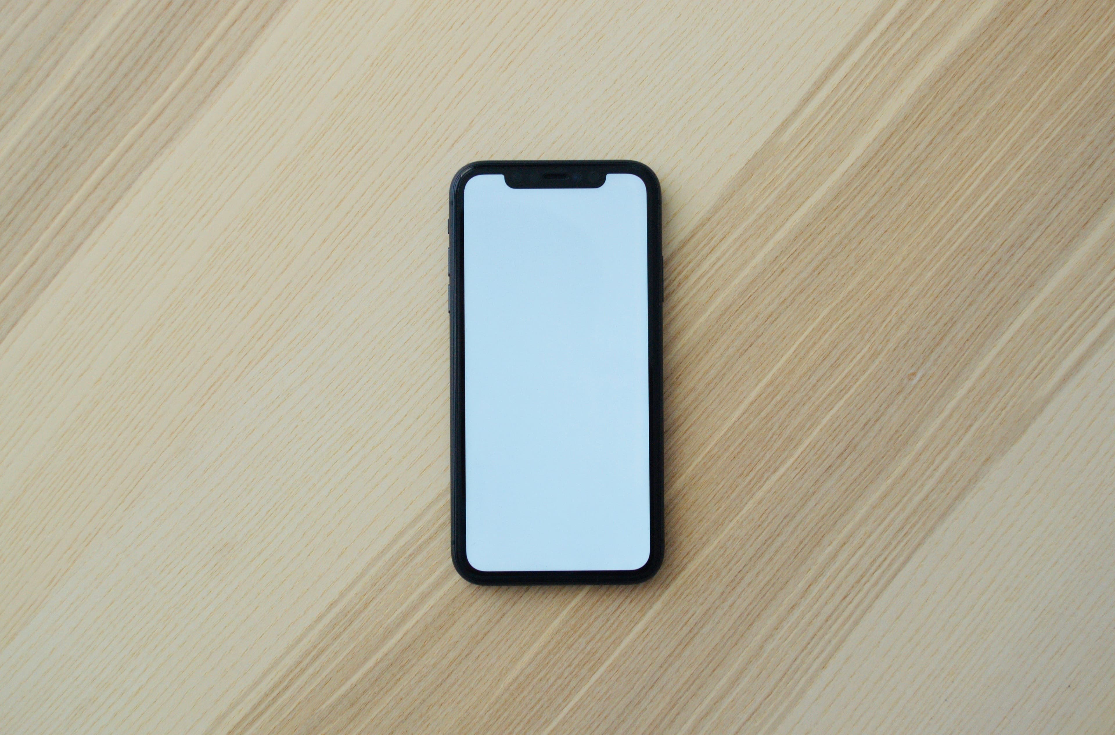Un smartphone noir à l'écran blanc vierge posé sur une surface en bois clair