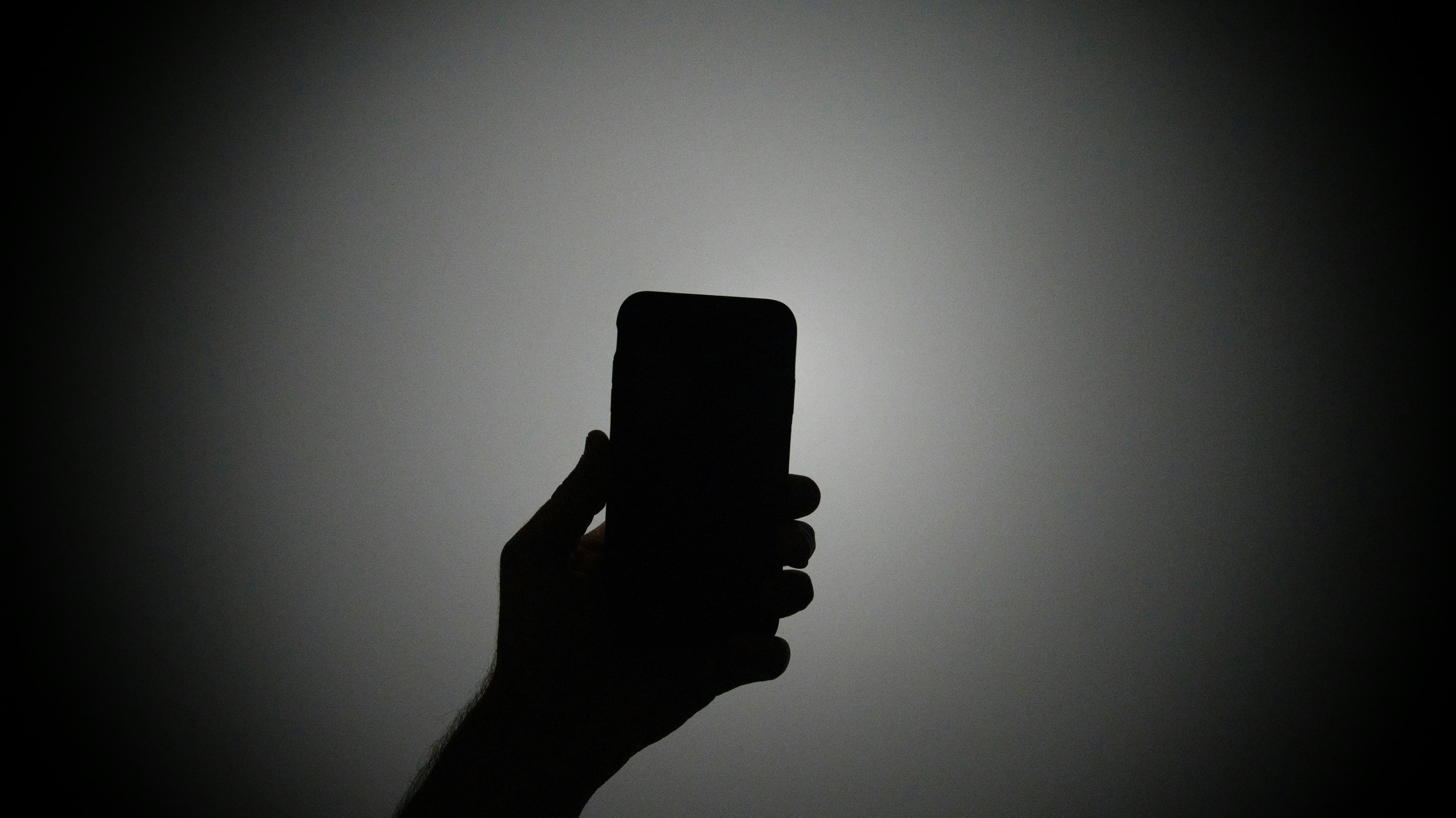 Silhouette d'une main tenant un smartphone allumé dans l'obscurité