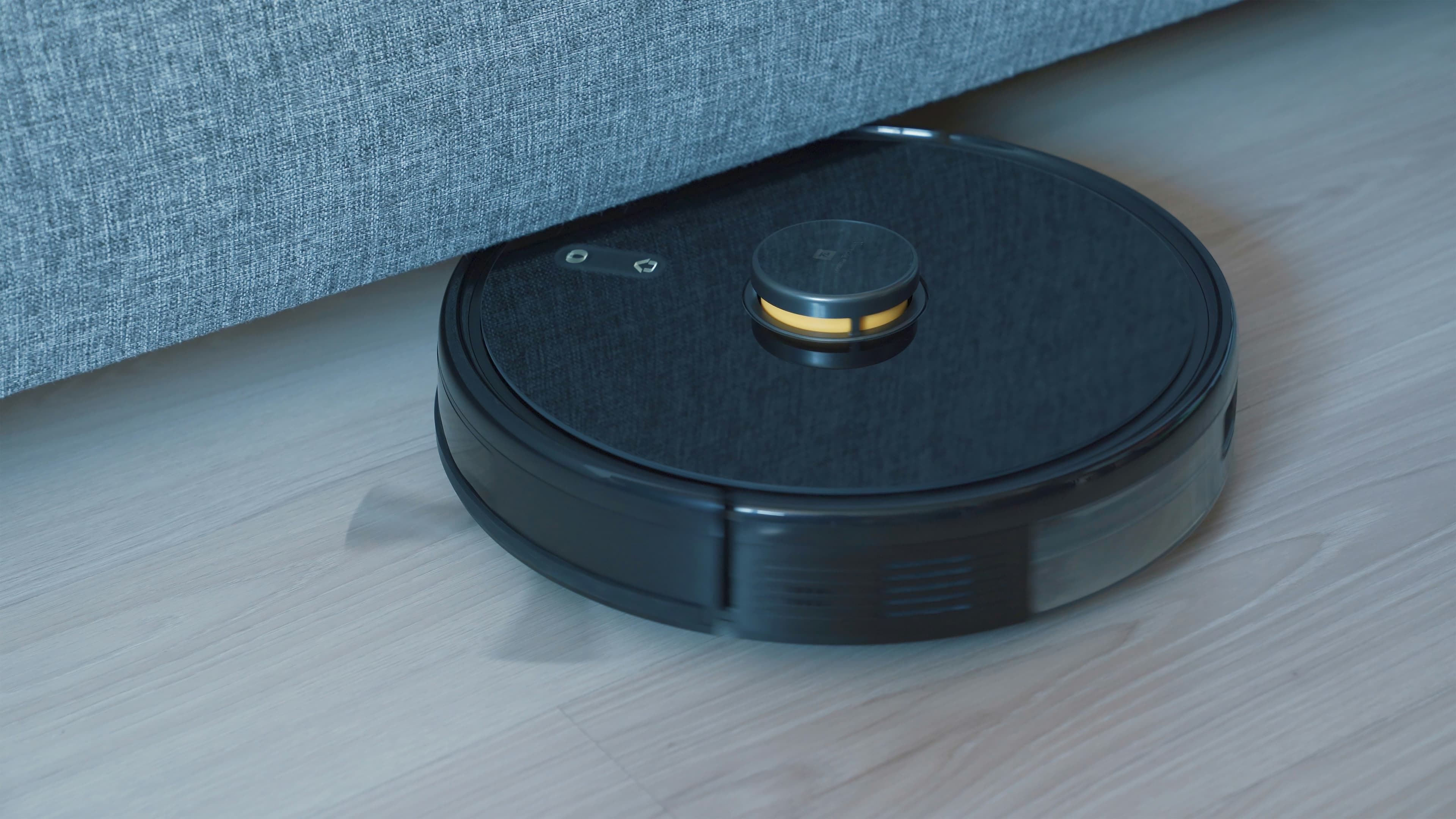 Un robot aspirateur noir posé sur un parquet en bois