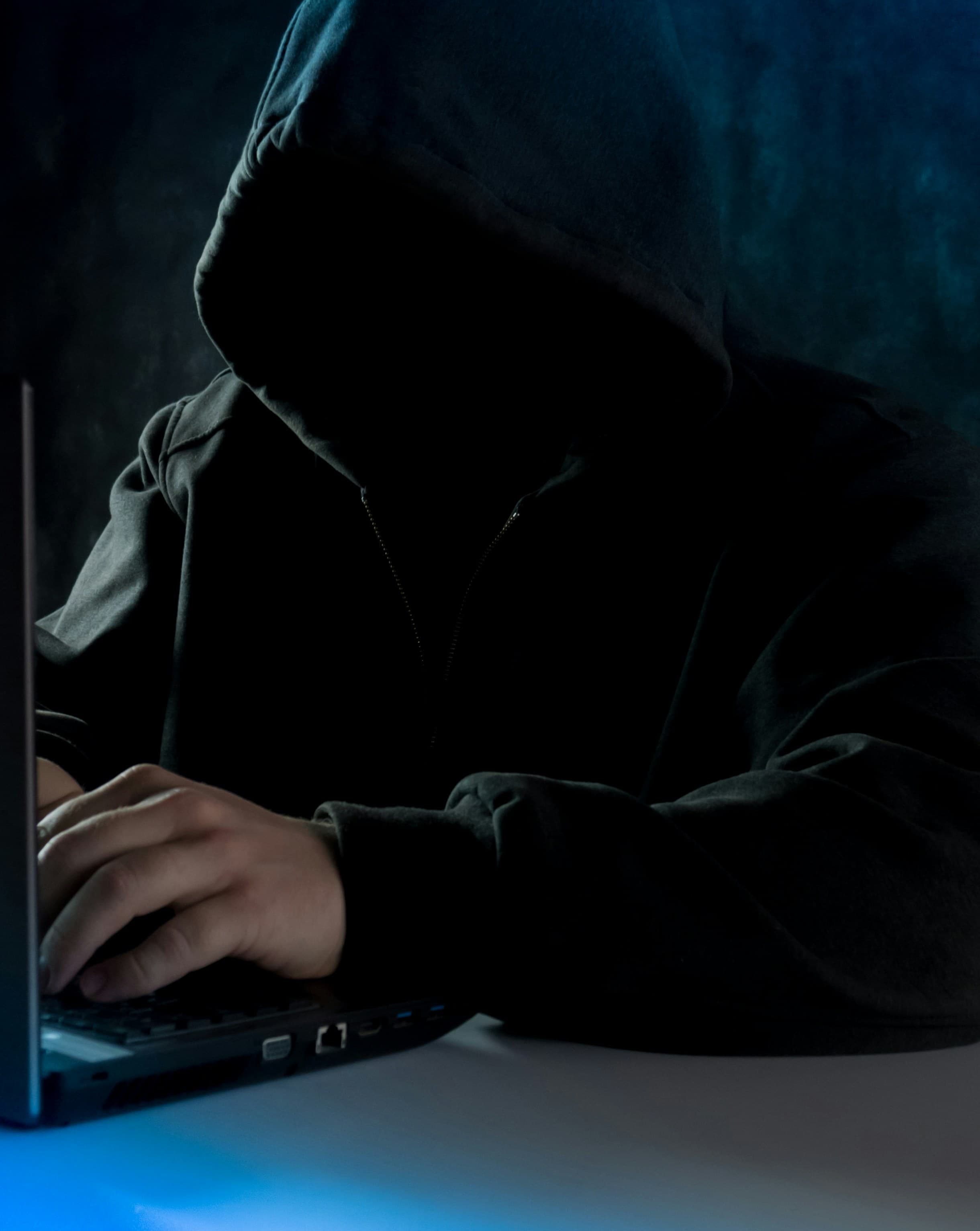 Personne encapuchonnée utilisant un ordinateur portable dans l'obscurité