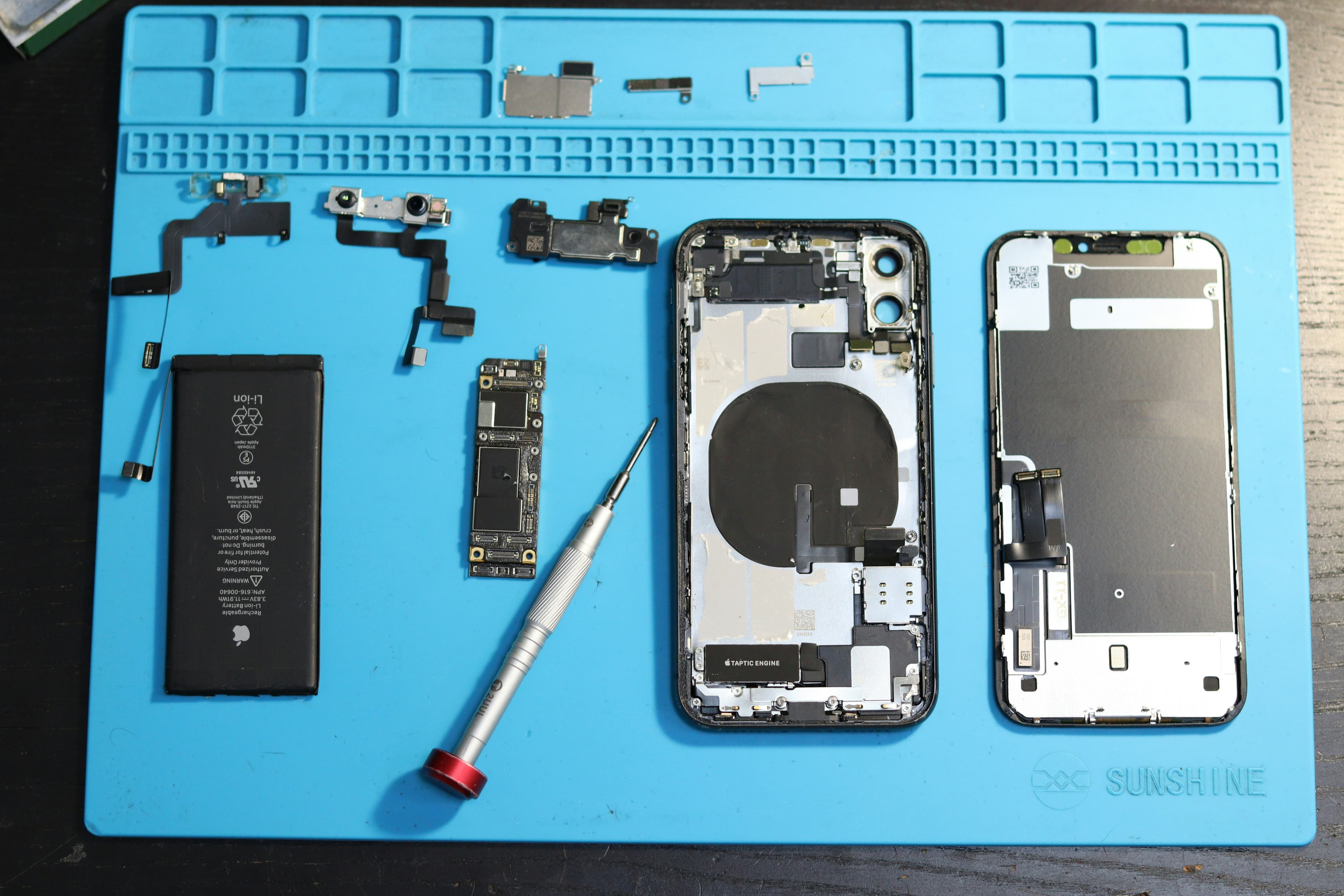 iPhone démonté avec ses composants disposés sur un tapis de réparation bleu