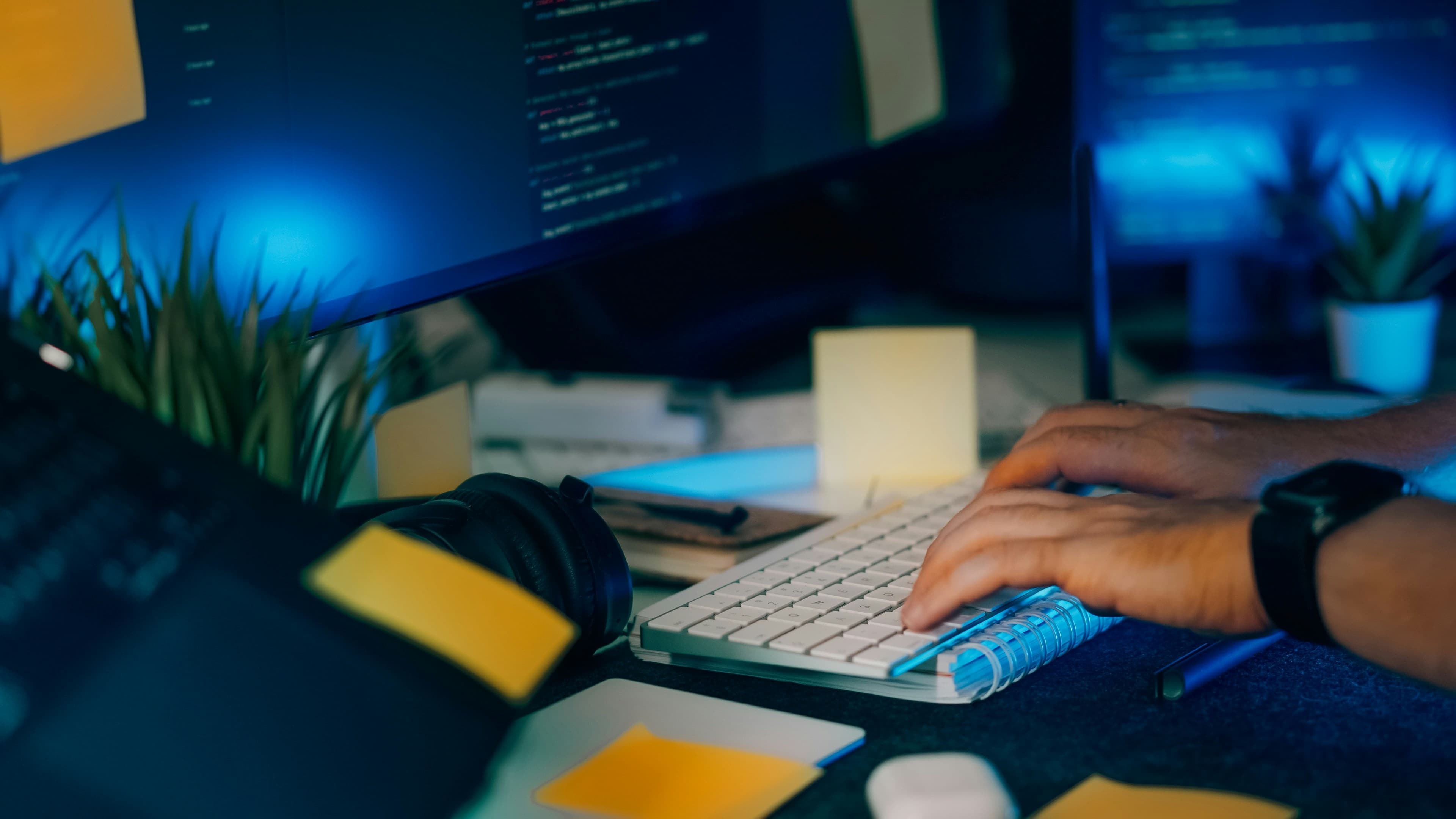 Mains tapant sur un clavier d'ordinateur devant des écrans affichant du code