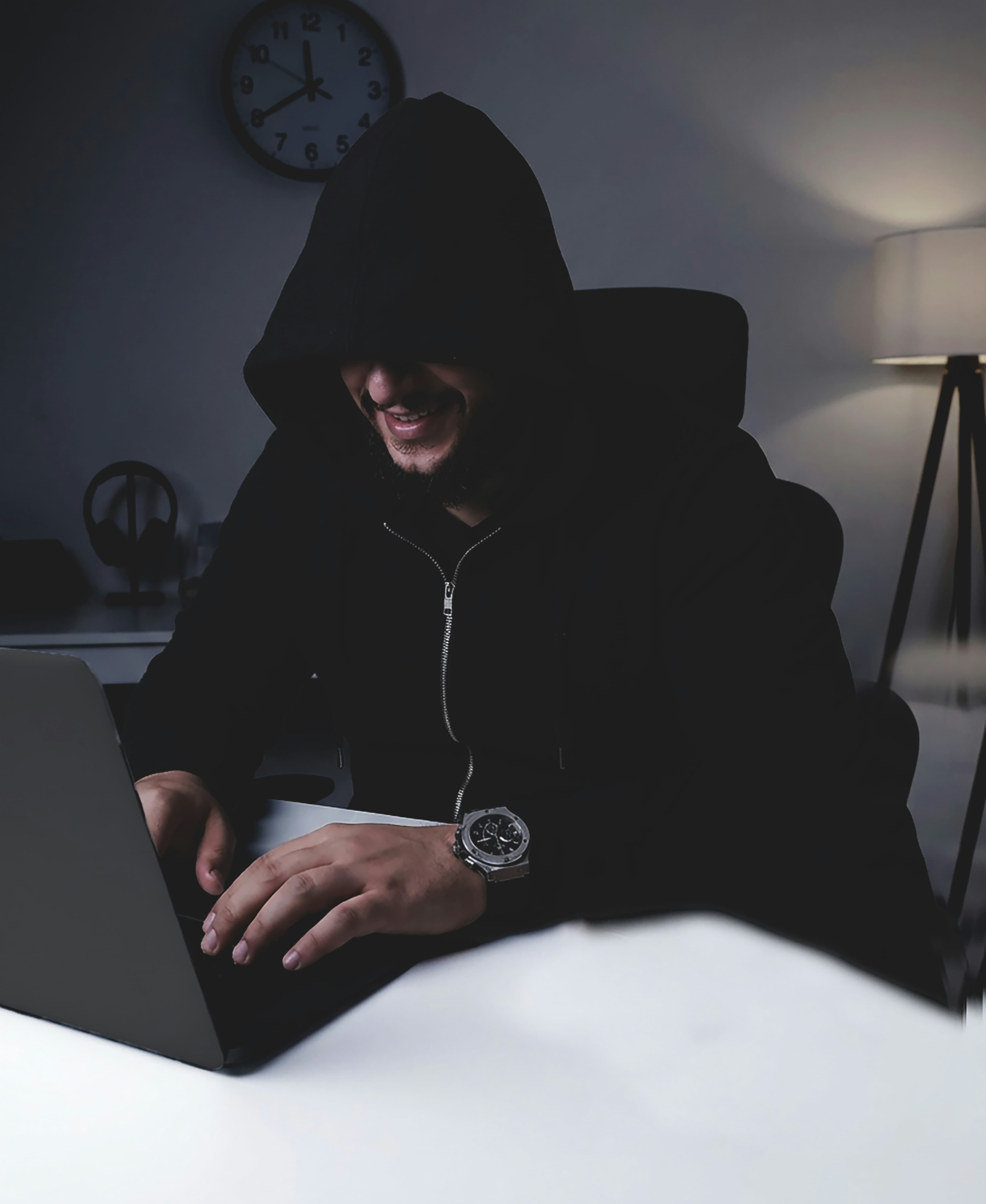 Personne en sweat à capuche travaillant sur un ordinateur portable la nuit, dans une pièce faiblement éclairée.