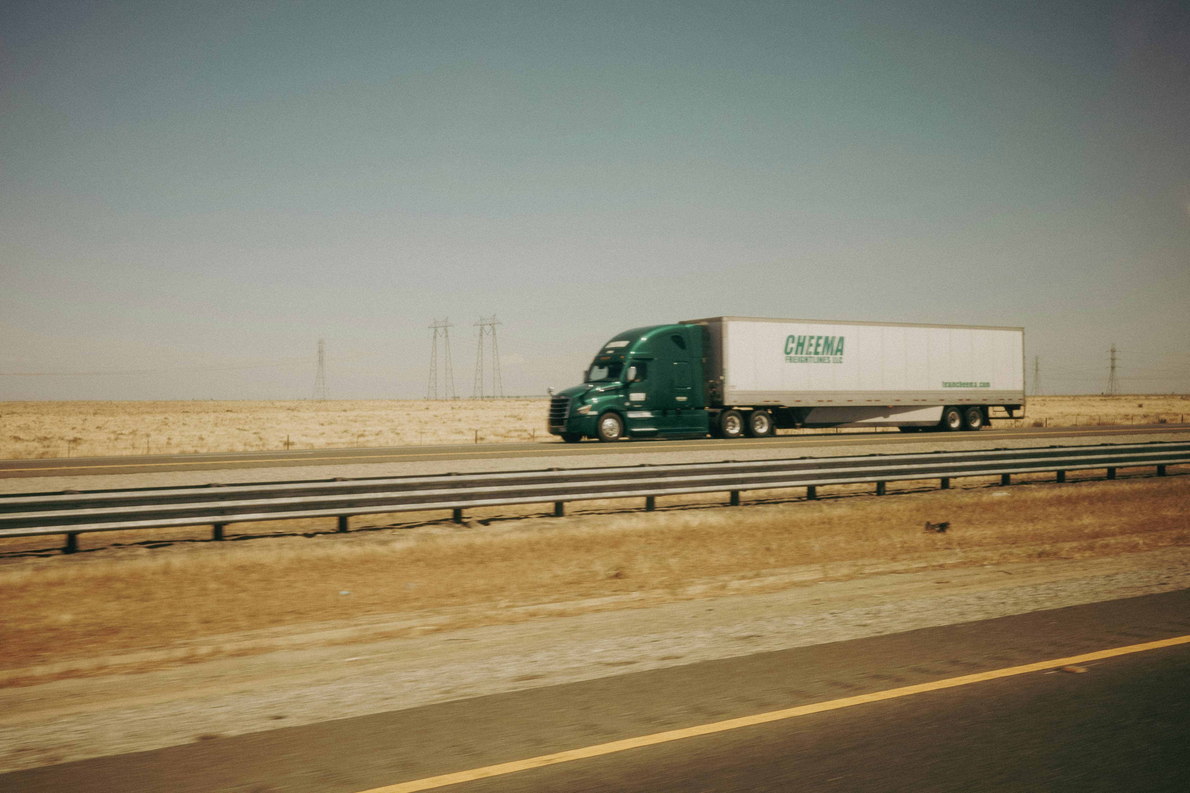 Un camion électrique vert circulant sur une autoroute désertique, avec des éoliennes à l'arrière-plan
