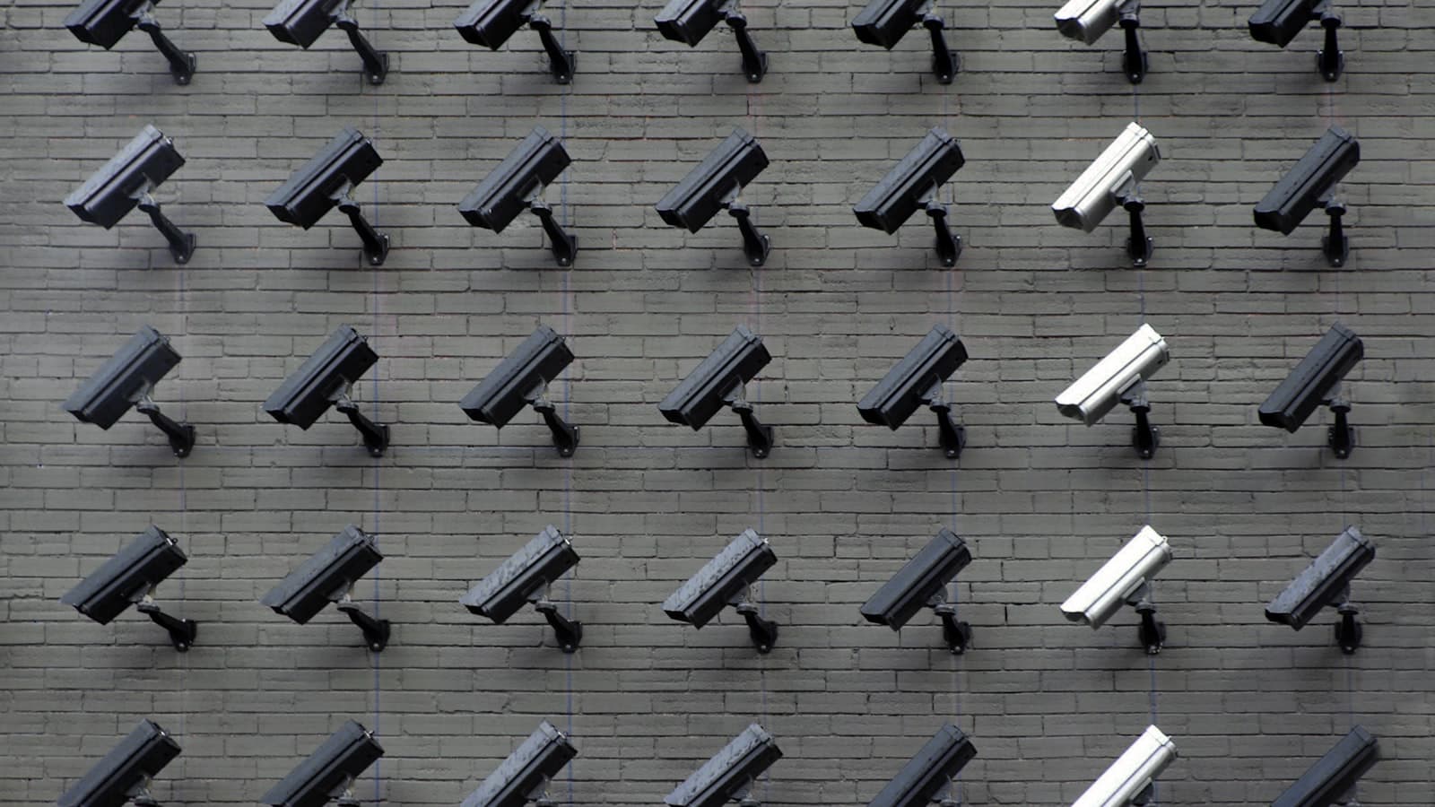 Plusieurs caméras de surveillance de couleurs différentes fixées sur un mur.