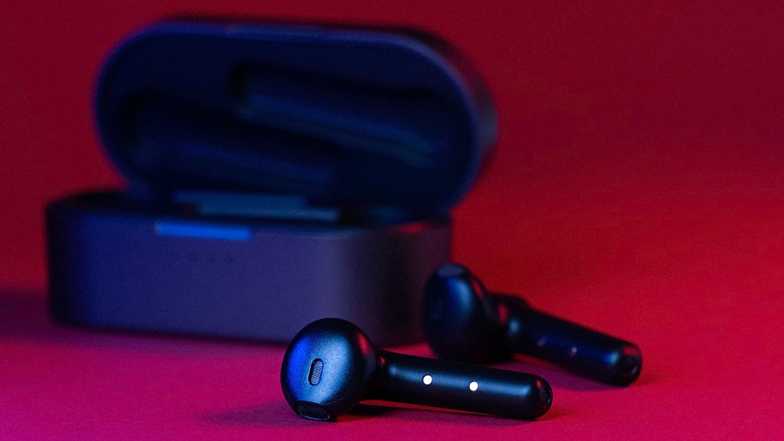 Une paire d'écouteurs sans fil noirs et gris posés à côté de leur boîtier de charge.