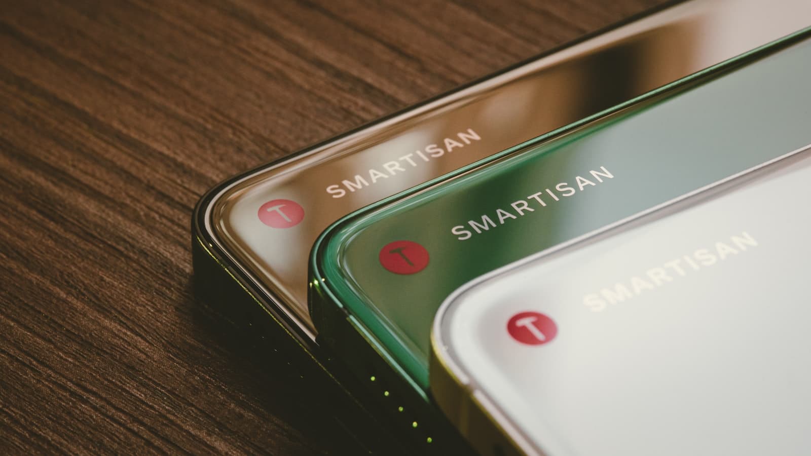 Trois smartphones de couleurs différentes posés côte à côte sur une table en bois.